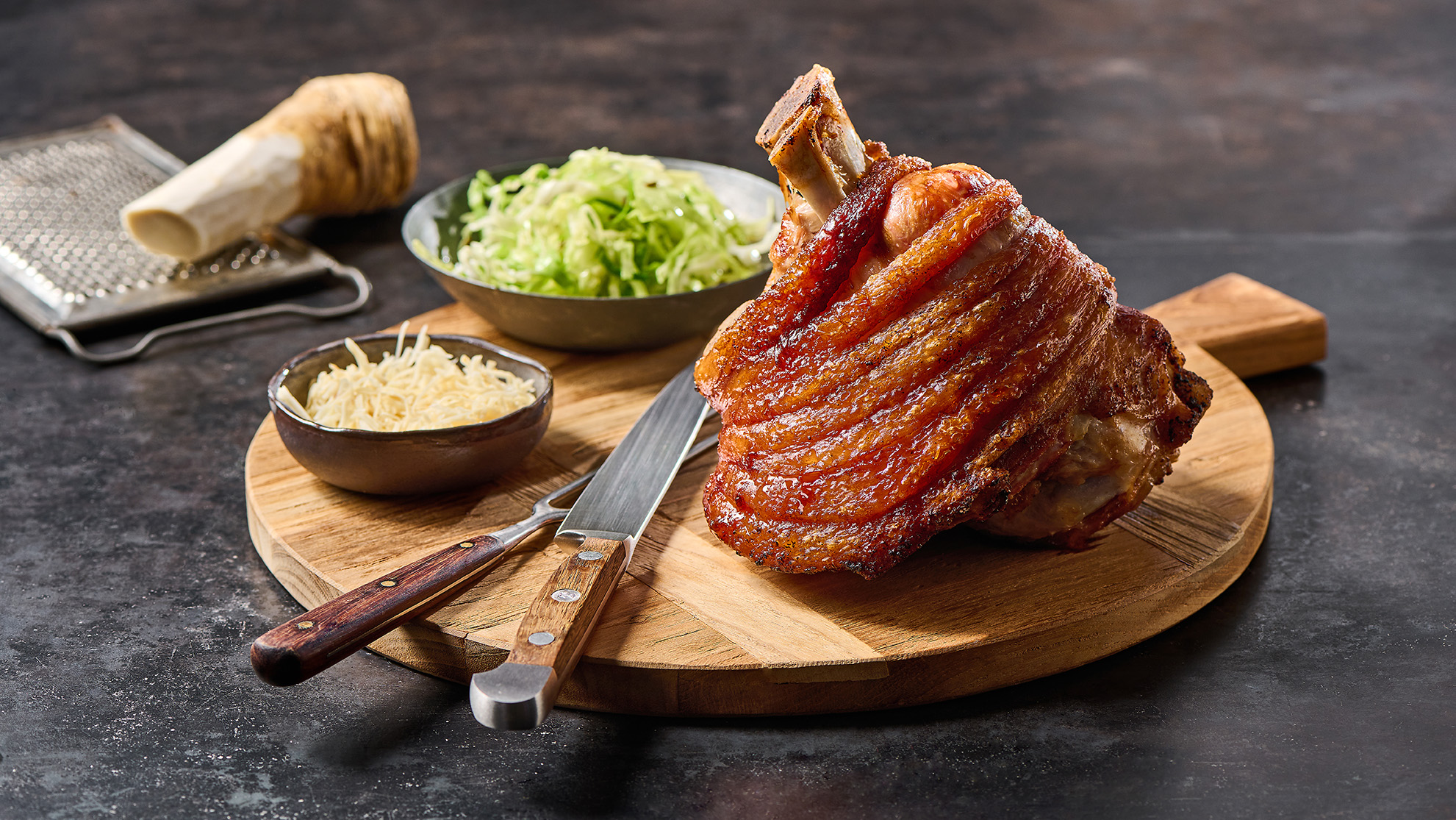 Knusprig gegrillte Schweinestelze mit Kren, angerichtet auf Schneidbrett mit Besteck